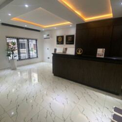 Modern Corporate Lobby With A Wooden Reception Desk, Marble Floors, Natural Light, And Sleek Minimalist Decor. Modern Corporate Lobby With Wooden Reception Desk, White Marble Floors, Natural Light, And Stylish Decor.