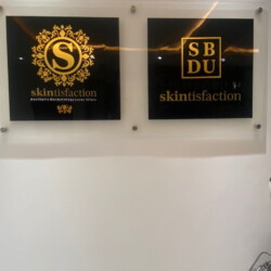 Modern Skincare Salon Wall Showcasing Elegant Gold And Black Skintisfaction Logos In Sleek Glass Frames. Modern Skincare Salon Wall With Luxury Gold And Black Skintisfaction Logos In Glass Frames.